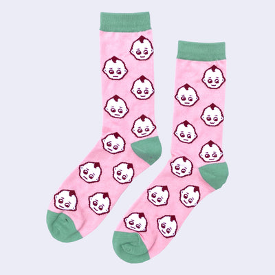 Pair of pink socks with sage green color accents around the toe, ankle and top. They have a repeating pattern of Kewpie heads, white with a burgundy outline.