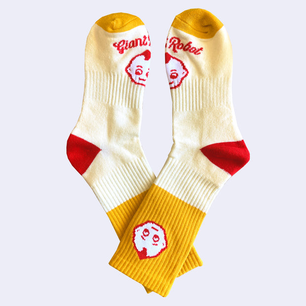 Pair of socks, mostly light yellow with a block of mustard yellow and red accents. A small kewpie head is on the ankle with another on the foot with "Giant Robot" written underneath.