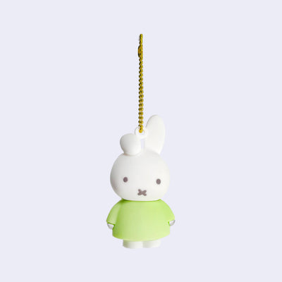 Rubber mascot figure of Miffy, wearing a light green dress with one of her bunny ears folded down. The figure is attached to a gold toned ball chain.