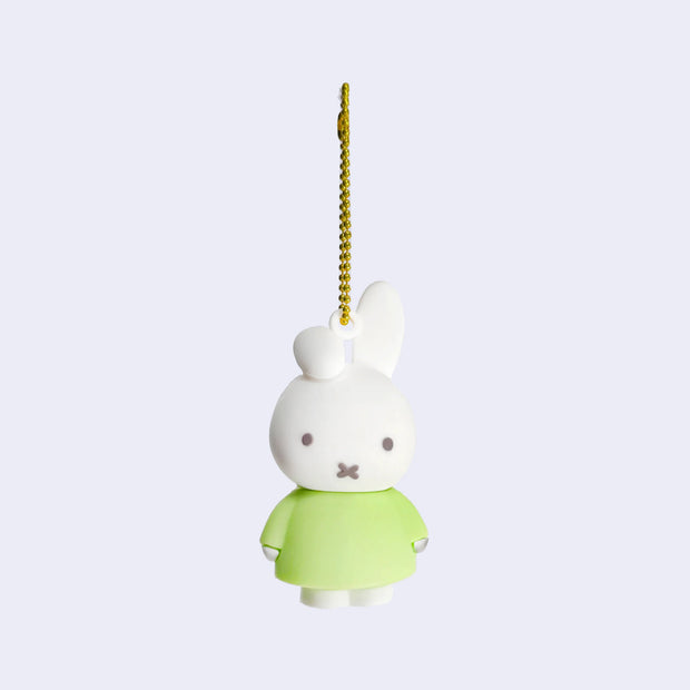 Rubber mascot figure of Miffy, wearing a light green dress with one of her bunny ears folded down. The figure is attached to a gold toned ball chain.