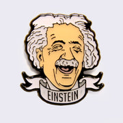 Enamel pin of an illustrated Albert Einstein head, smiling with eyes closed and a scroll banner below that reads "Einstein" in all caps. 